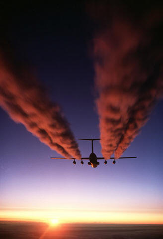 A plane flying at sunset, its contrails colored pink